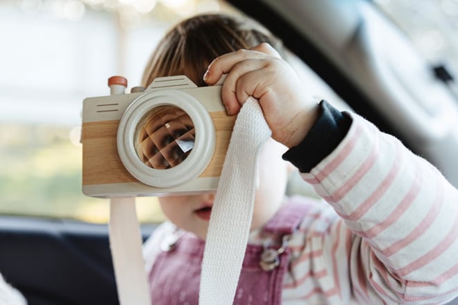Photo of a toddler holding up her own toy camera, inside a car 