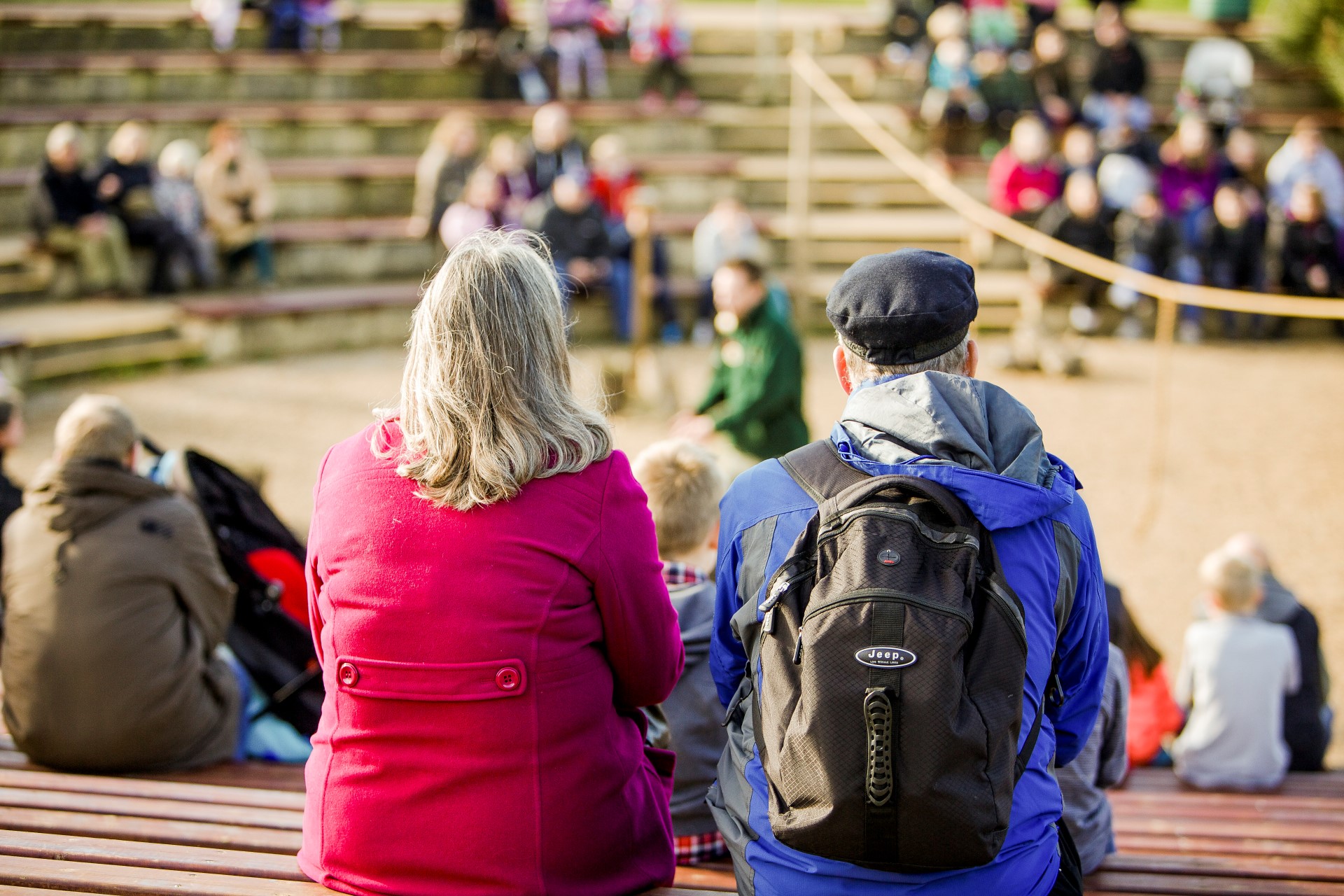 Man and woman sit and watch bird demonstration with surrounding crowd in Ampitheater 