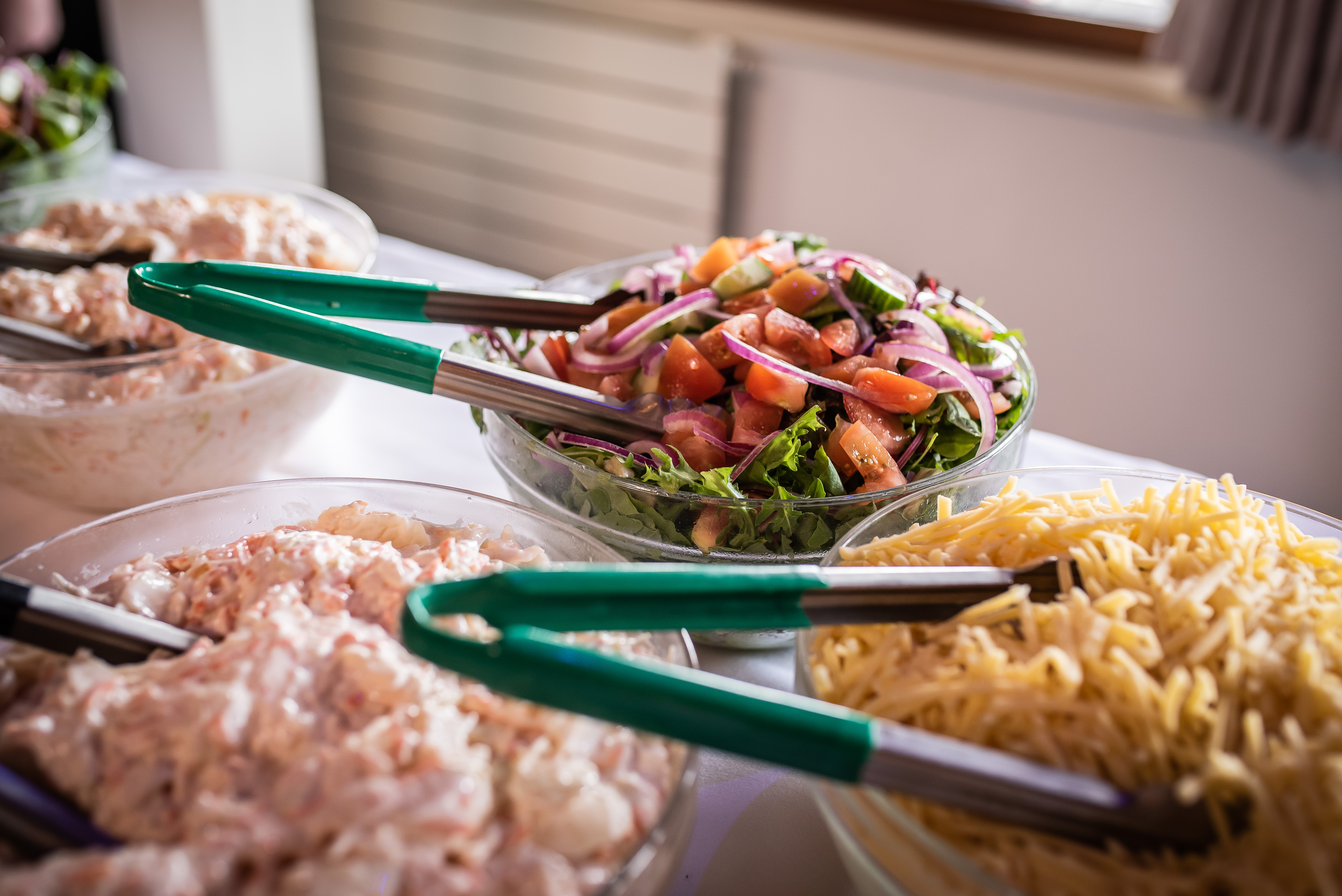 Salad and fries laid out on a buffet table with tongs in the bowls 